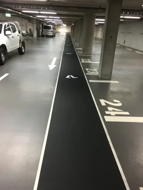 Black pedestrian walkway with white outline and numbered bays in an underground Sydney car park