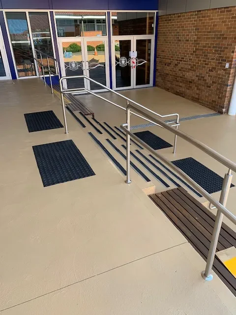 Tan sealed concrete ramp and stairs with tactile indicators at a school entrance