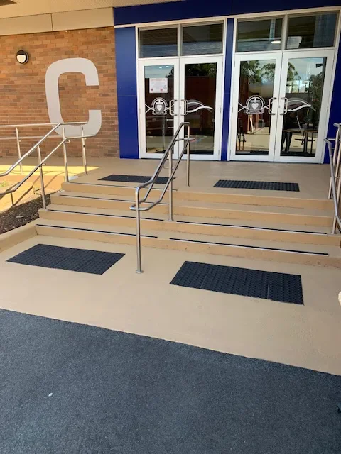 Light tan sealed concrete stairs and ramp with stainless steel handrails at a school entrance