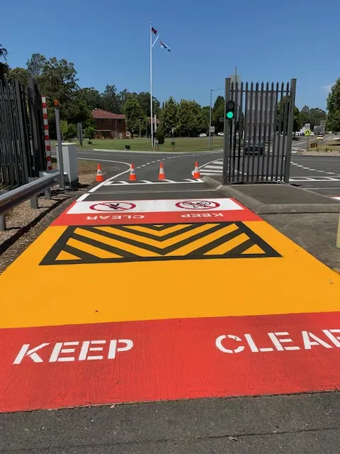 Red keep clear markings with yellow hazard chevrons at a defence facility security gate