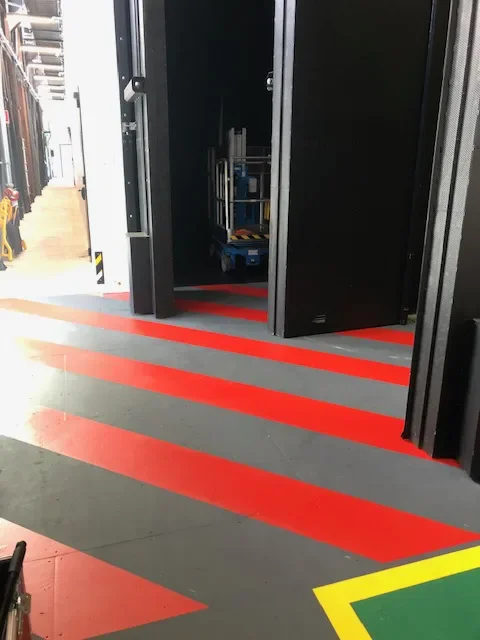 Red diagonal hazard stripes and green bordered safety zone on an industrial floor